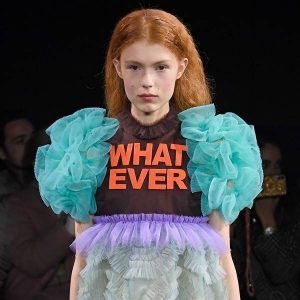 a model in the Viktor & Rolf Spring 2019 Couture runway show in Paris featuring lots of tulle dresses bearing slogans, this one says "Whatever"